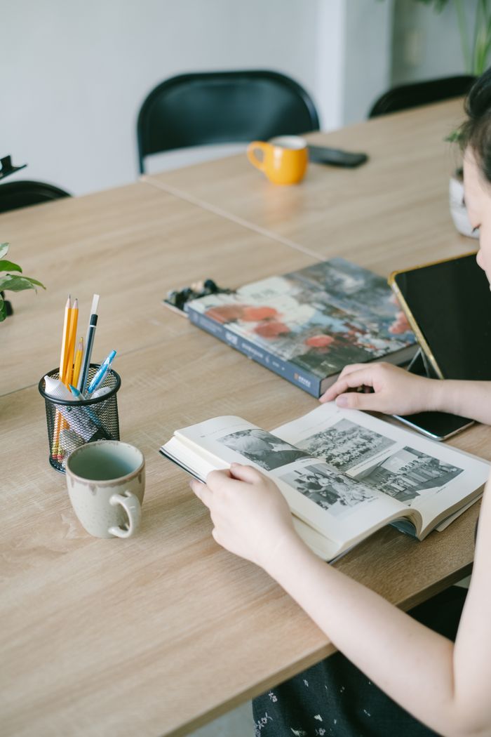 A young woman concentrating on reading a book at a wooden desk with coffee and stationery.